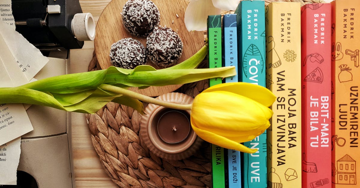 'Tony Stonem' type in classical literature - Top view stack of books on table near beautiful yellow tulip and orchid flowers arranged with chocolate truffles placed on wicker placemat