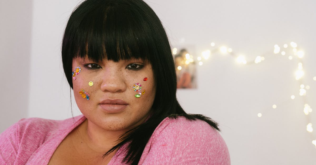 Appearance of a boggart to someone who is most afraid of boggarts - Tender young ethnic overweight lady with black hair and colourful glitter on face wearing pink shirt standing in light decorated room and looking at camera