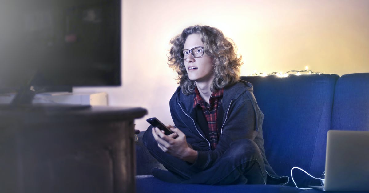 Are fictional trademarks or brand names used in movies and TV legally held? - Concentrated male with long hair sitting on comfortable sofa at home and messaging on social media via cellphone while watching movie on TV with opened mouth
