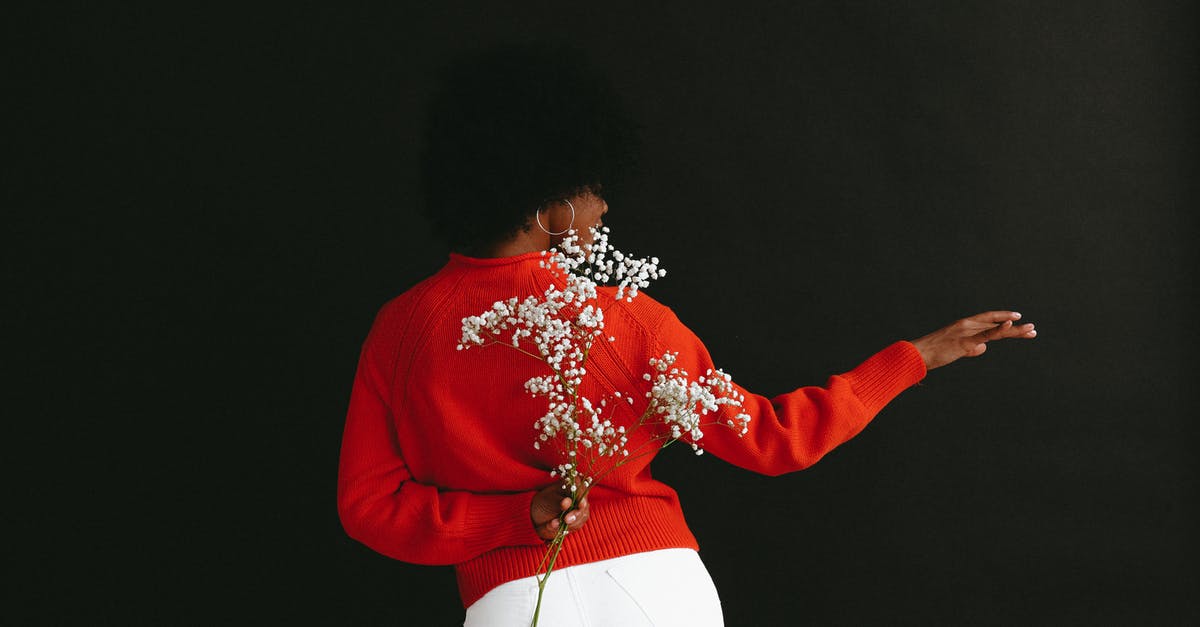 Are modern black & white movies shot in colour? - Back view of sensual black woman in white denim and white red sweater holding Gypsophila flower behind back posing on black backdrop