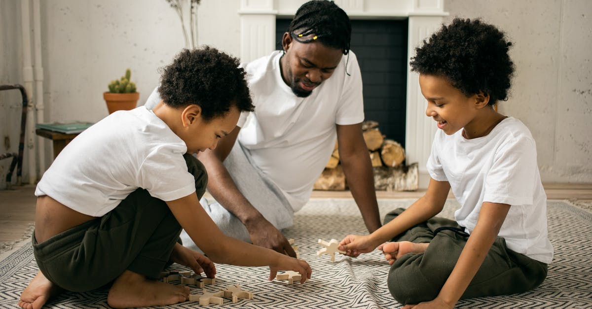 Are Ray and Emmit Stussy twin brothers? - Happy young African American father in casual outfit smiling while sitting on floor and playing with wooden toys with positive twin sons during weekend at home