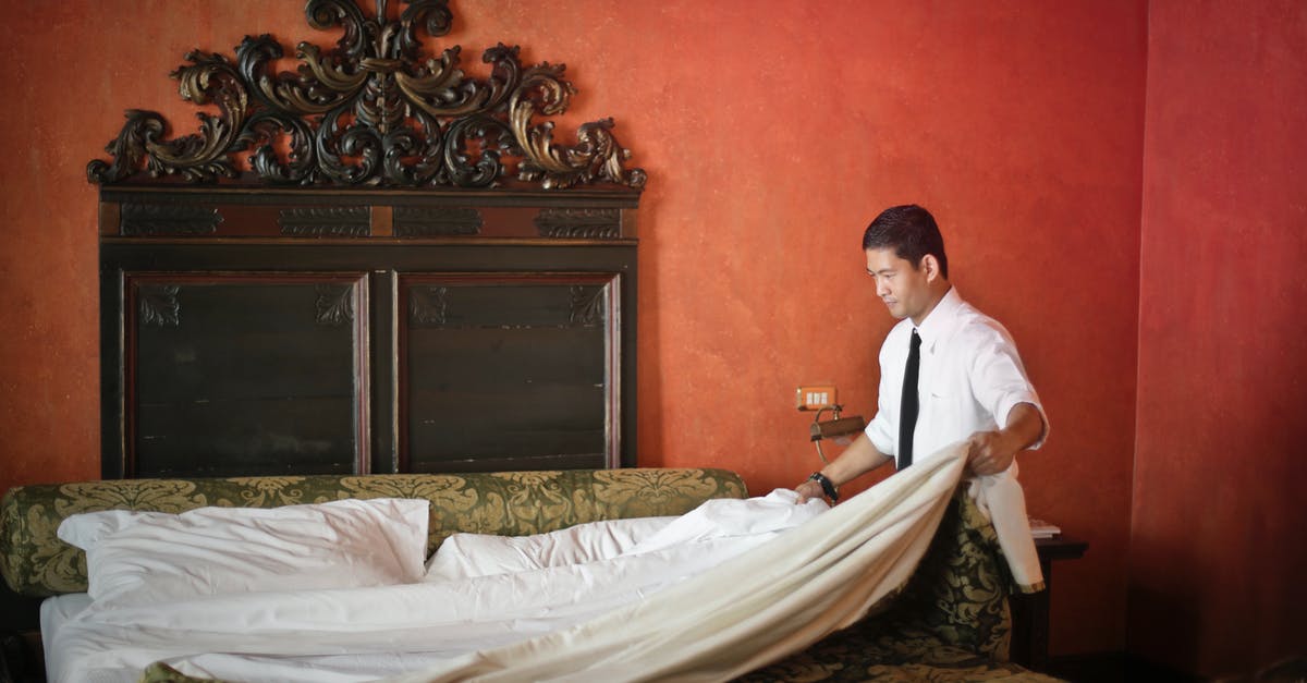 Are the Clean Shaven Officer and the Old Man supposed to be the same person? - Side view of young ethnic male making bed while cleaning stylish hotel room with vintage furniture and red walls