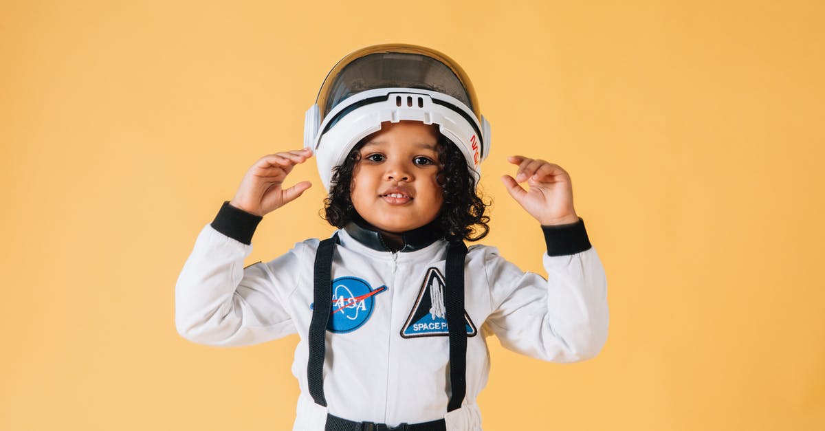 Are the performances on Glee largely the characters' imagination? - Cheerful little African American girl wearing white astronaut spacesuit and helmet and looking at camera contentedly while standing against brown wall