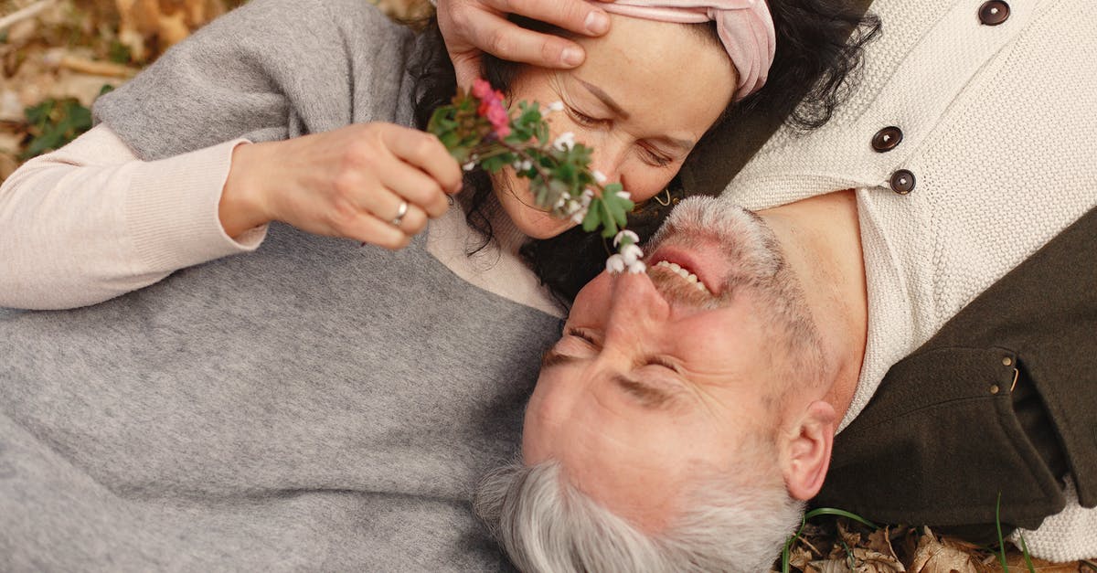 Astronaut rescues corrupted wife from hell [closed] - From above of cheerful senior wife wearing wide scarf and headband with flower bouquet in hand and happy elderly gray haired husband in warm clothes lying on ground with fallen leaves in park with closed eyes