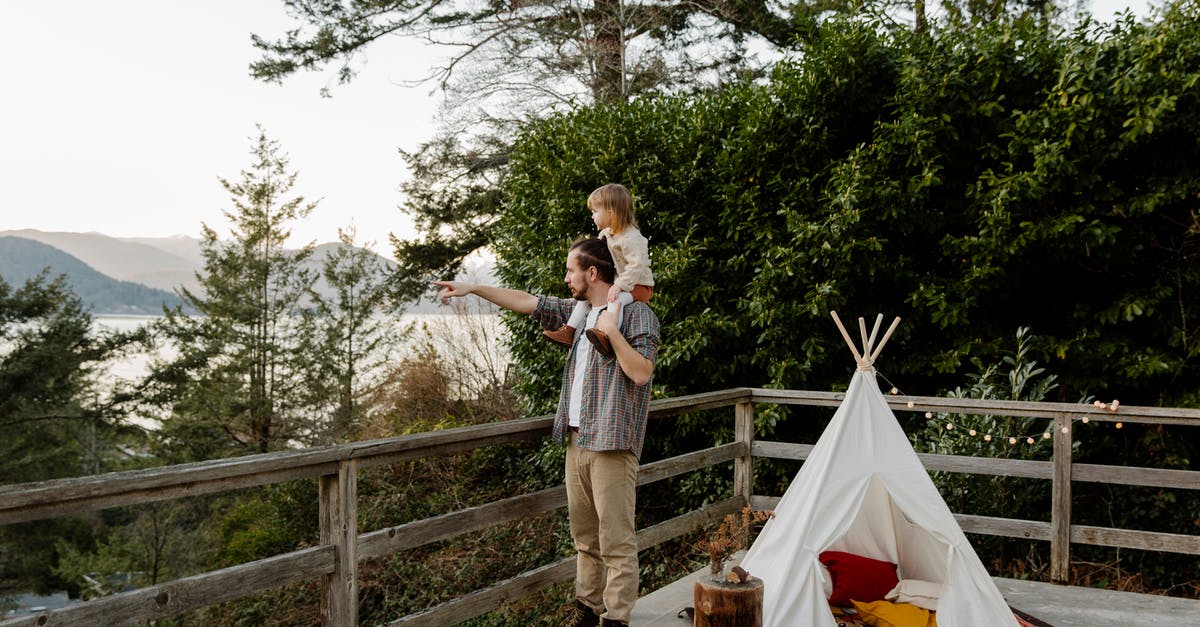 At what point in E.T. do E.T and Elliot begin to 'bond'? - Side view of little child sitting on shoulders of father while man pointing to mountain while standing on wooden terrace with wigwam and picturesque view