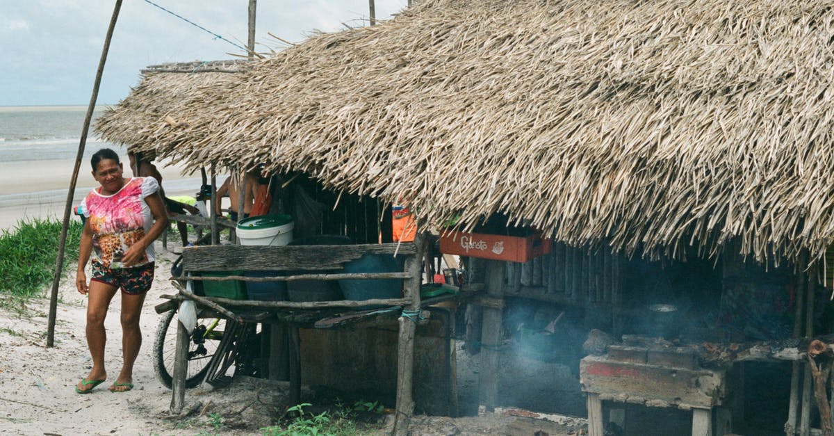 Authentic Standard Life campaign? - Ethnic woman walking at small hut with thatched roof in local poor village on ocean shore