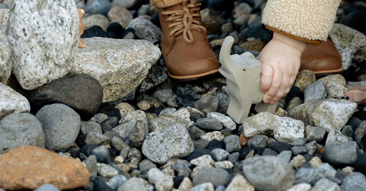 Baby at the end True Detective season 2 - Unrecognizable little child in warm clothes and brown boots playing with stone toy of elephant between stones on seashore in winter