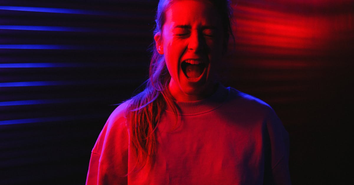 Bourne Legacy and Paranoia? - Frightened young woman standing with closed eyes and screaming in dark room with colorful neon lights