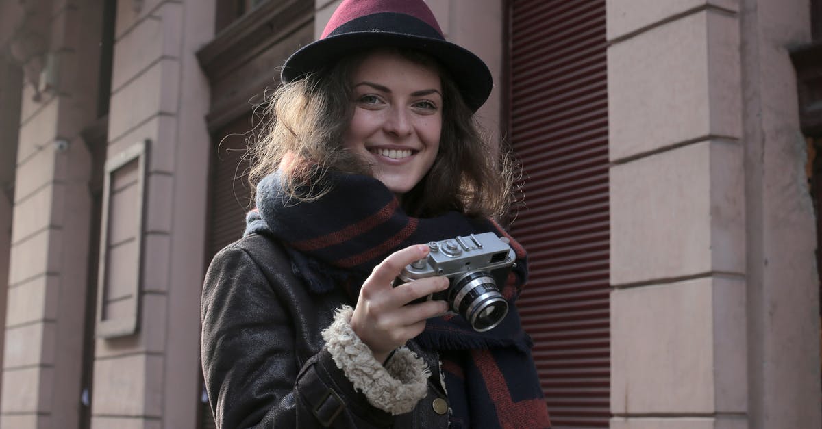 Camera shot with close-up next to farther away standing person - Woman in Black Jacket Holding Black Camera