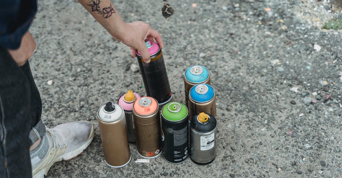 Can a specific shooting style be patented? - Crop anonymous person in sneakers with tattoo and heap of multicolored spray paint cans on ground standing on street in city
