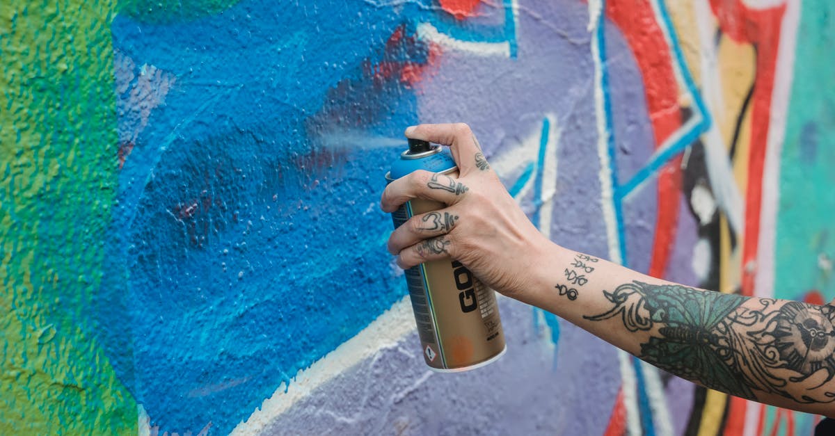 Can a specific shooting style be patented? - Crop unrecognizable tattooed painter spraying blue paint from can on multicolored wall with creative graffiti while standing on street in city
