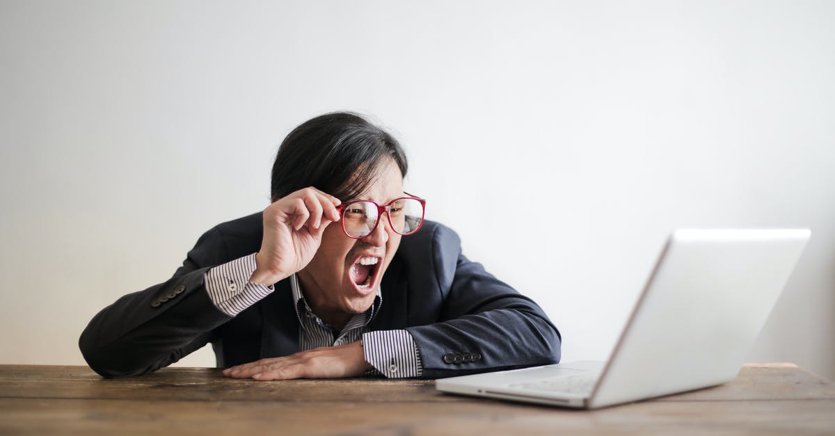 Can Wonder Woman die? - Modern Asian man in jacket and glasses looking at laptop and screaming with mouth wide opened on white background