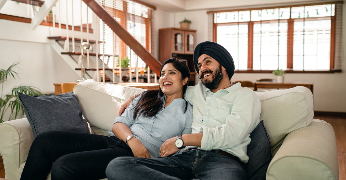 Chained up in the basement movie, comedy (maybe)? [closed] - Happy young Indian man in turban and positive woman in casual clothes embracing and laughing while watching comedy movie sitting on sofa