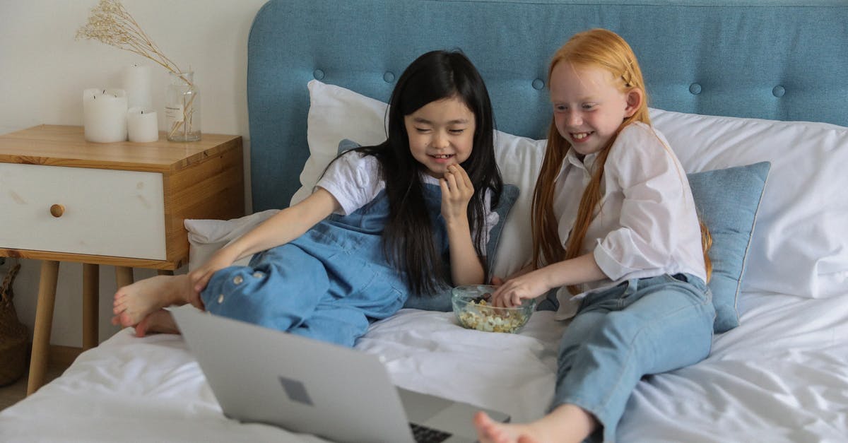 Comedy spy movie (probably with Leslie Nielsen) [closed] - Full body of happy barefooted diverse children with long hairs lying on comfortable bed and eating popcorn while watching funny cartoon on laptop in cozy room
