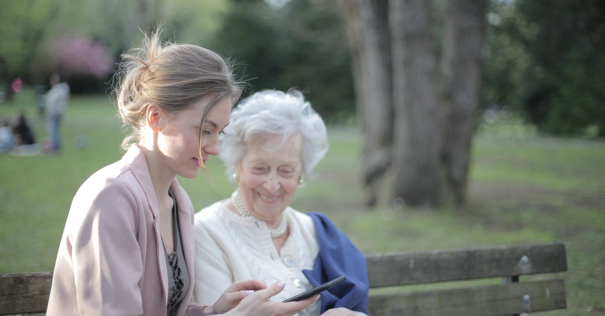 Connection between Children in Supernatural - Side view of smiling adult female helping aged mom in using of mobile phone while sitting together in park