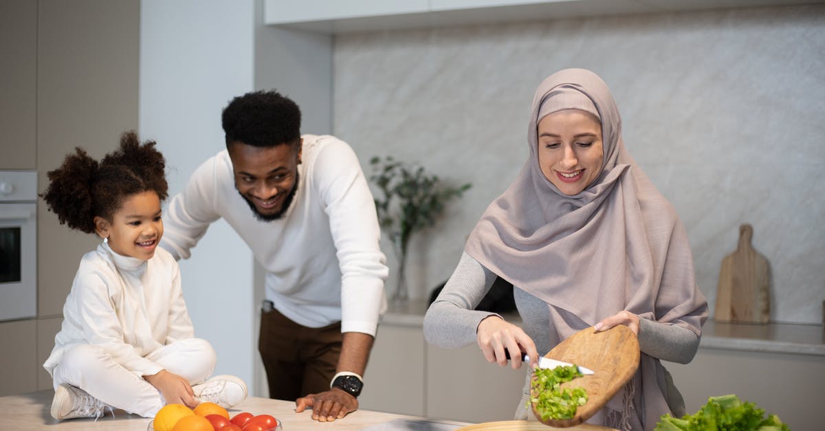 Cut scene reference, Family Guy's Chris is a reptile - Cheerful young African American father and daughter looking at Muslim mother cutting green salad while cooking in kitchen at home