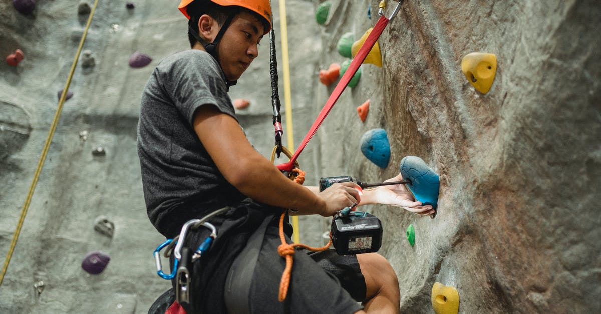 Did Andy Dufresne use more than one rock hammer to escape from Shawshank? - From below side view of attentive young Asian climber in protective helmet using electric screwdriver on hold of artificial rock