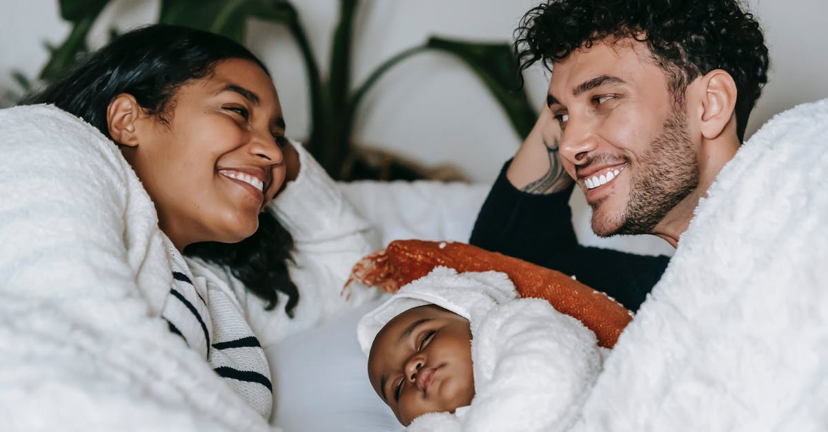 Did Ben and Chon know about each other sleeping with O? - Happy ethnic couple lying with baby on bed in bedroom
