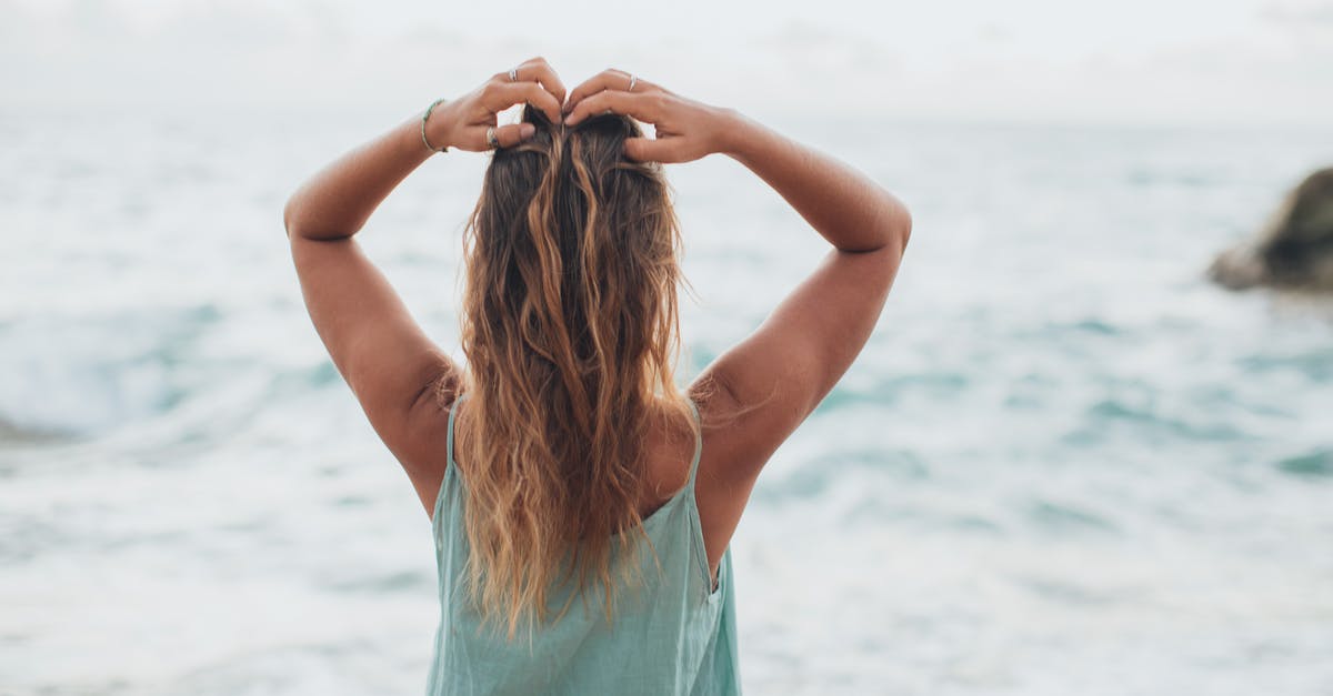 Did Rapunzel's hair get the power back? - Back view of unrecognizable female in light top admiring powerful waving ocean with raised arms during summer holidays