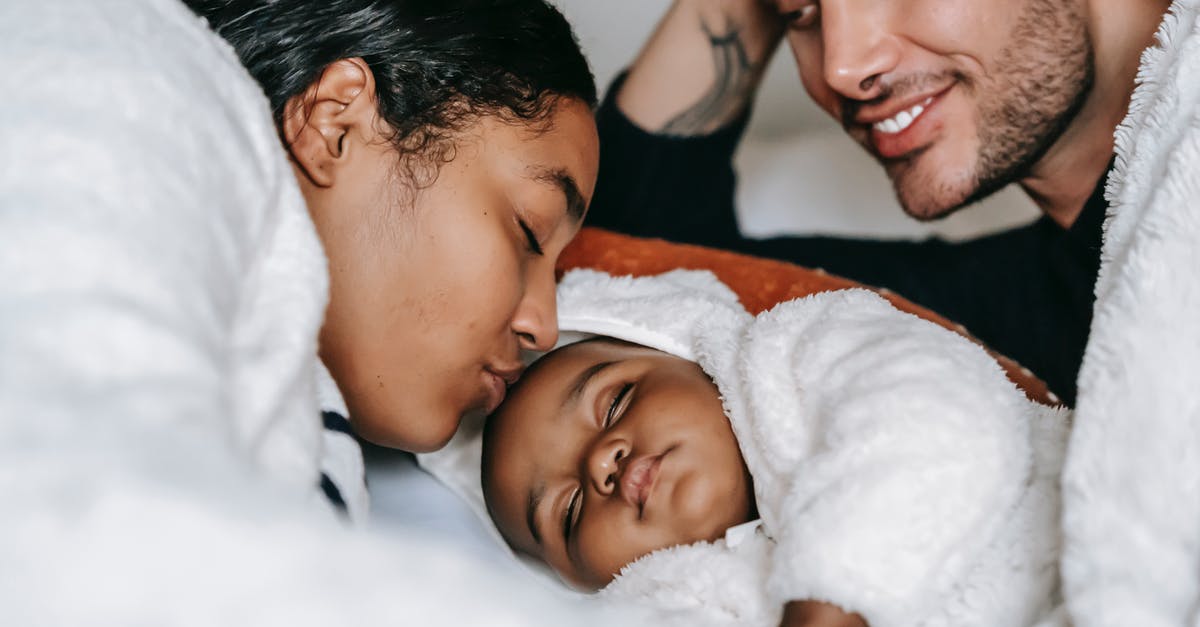 Did Tony lie about his father's death? - High angle of crop young African American woman kissing sleeping cute newborn baby while resting in bed with happy husband