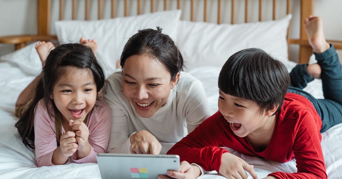Do I have to watch The Bourne Legacy to watch Jason Bourne? - Full body happy Asian mother pointing at screen tablet showing interesting information to cheerful kids while lying on cozy bed in light room