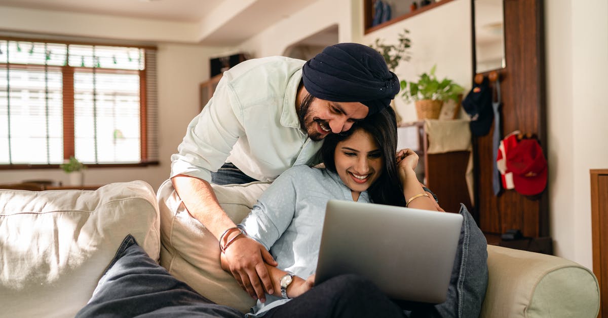 Do Indian movies screened outside India, have intervals as well? - Cheerful man bending over sofa and putting hand on hand of ethnic wife sitting with laptop while looking at screen together in living room