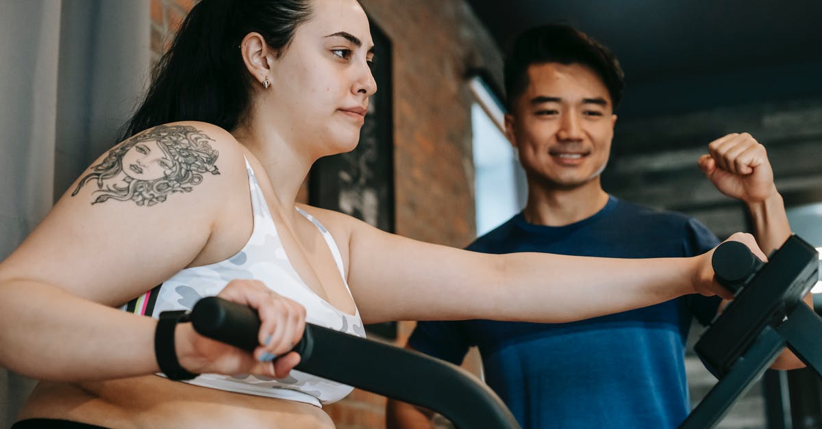 Do King Benny and Fat Man know the whole story? - From below of happy young Asian male trainer motivating exhausted young female client to to cardio fat burning exercise on elliptical machine in modern sport club