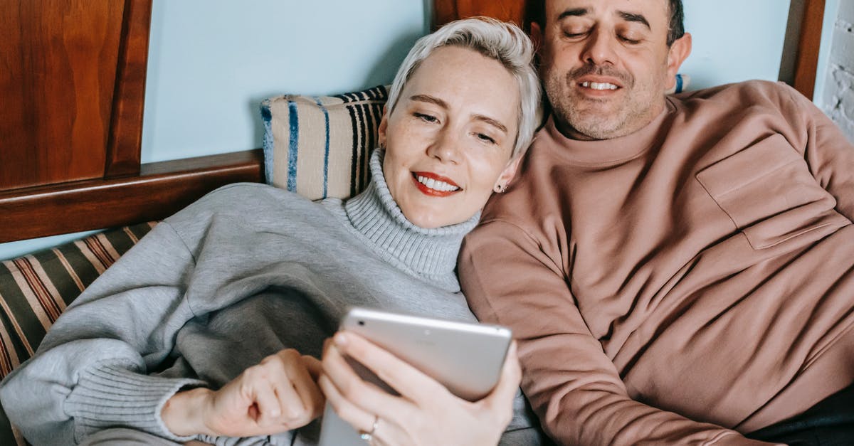 Do movie soundtracks video clips follow the movie's age rating? - Content diverse middle aged married couple in warm casual clothes lying together on bed and smiling while watching movie on tablet