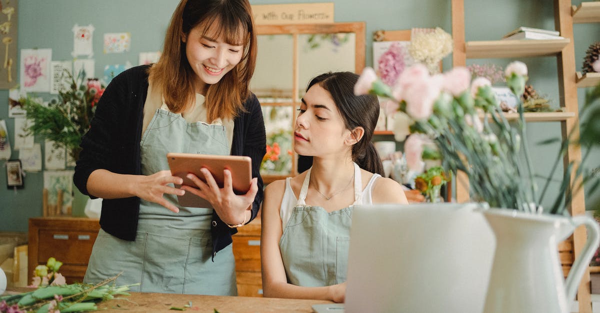 Do the maids' apron designs indicate position? - Content multiethnic female coworkers at table with flowers surfing tablet while choosing design for bouquet during work in florist shop