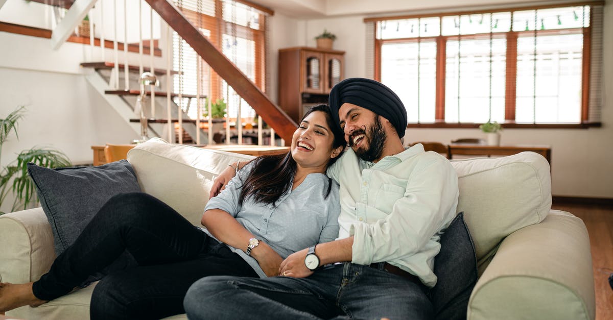 Does a horror movie have to have supernatural elements? - Happy young Indian couple laughing and cuddling while relaxing on couch