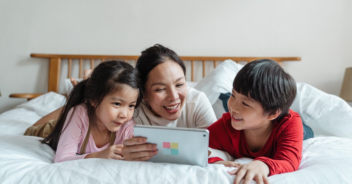 Does a horror movie have to have supernatural elements? - Cheerful ethnic mother watching video via tablet with kids on bed