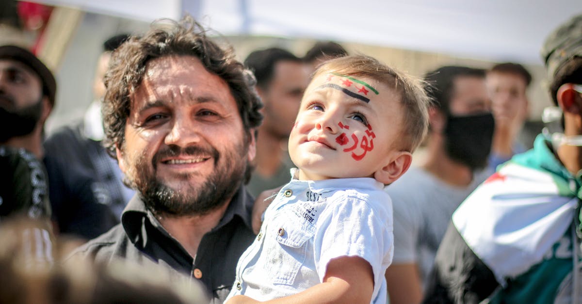 Does Carrie know about the drone strike Walden authorised - Ethnic bearded man carrying small kid with painted face in crowd of protesting against policy