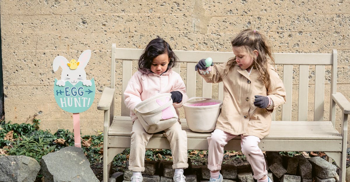 Does Charlotte have siblings? - Full body positive cute diverse girls in warm clothes playing with Easter eggs and sitting on bench in backyard