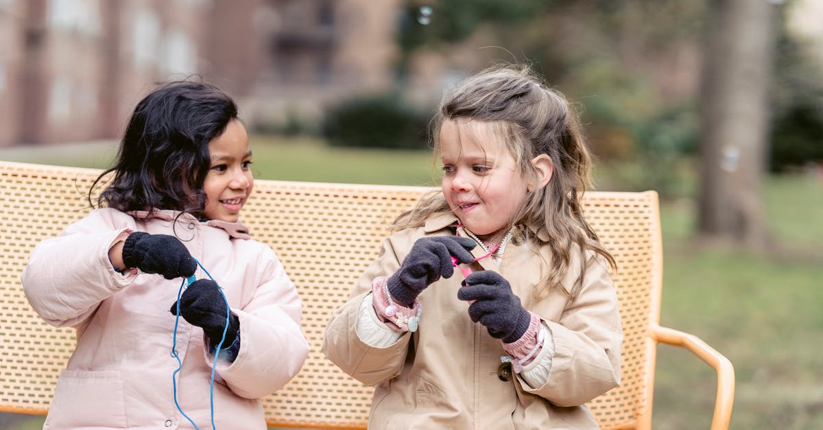Does each season of Dexter have an overarching theme? - Happy multiracial girls wearing warm jackets playing with soap bubbles and looking at each other while sitting on bench in spring garden