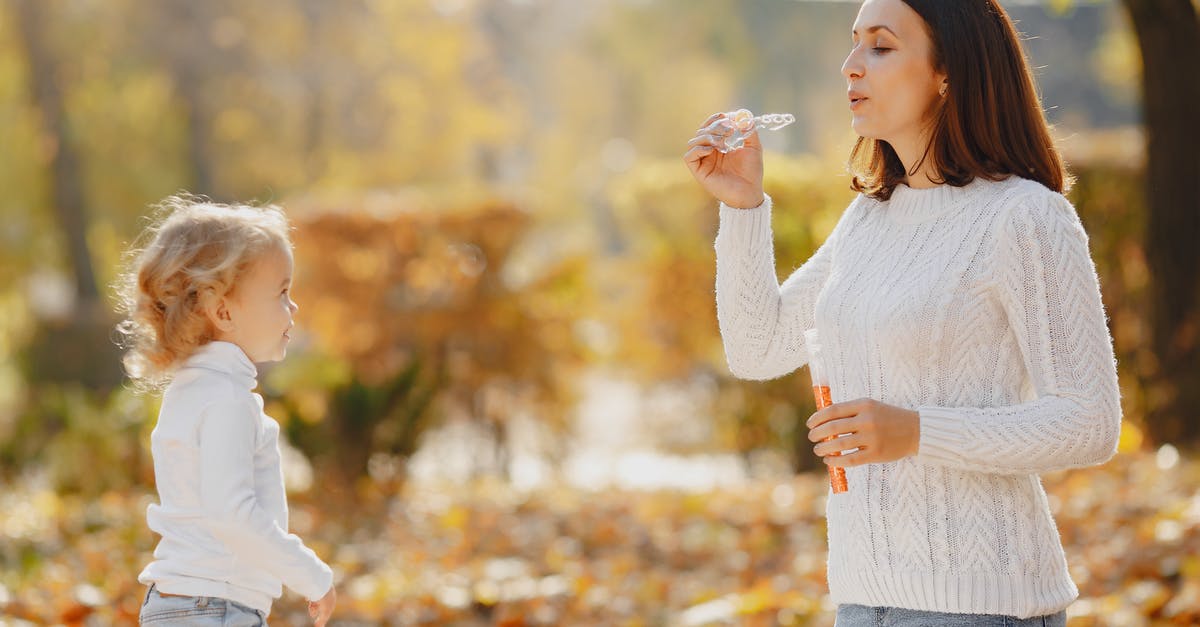 Does each season of Dexter have an overarching theme? - Side view of mother and child in warm sweaters standing opposite each other and playing while blowing soap bubbles in autumn park