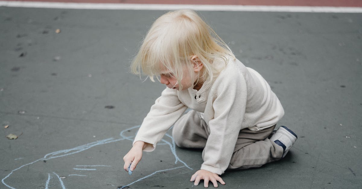 Does Junior perceive he is being condescended to/not taken seriously as boss? - From above of adorable focused little kid in casual wear sitting on asphalt ground and drawing with chalk