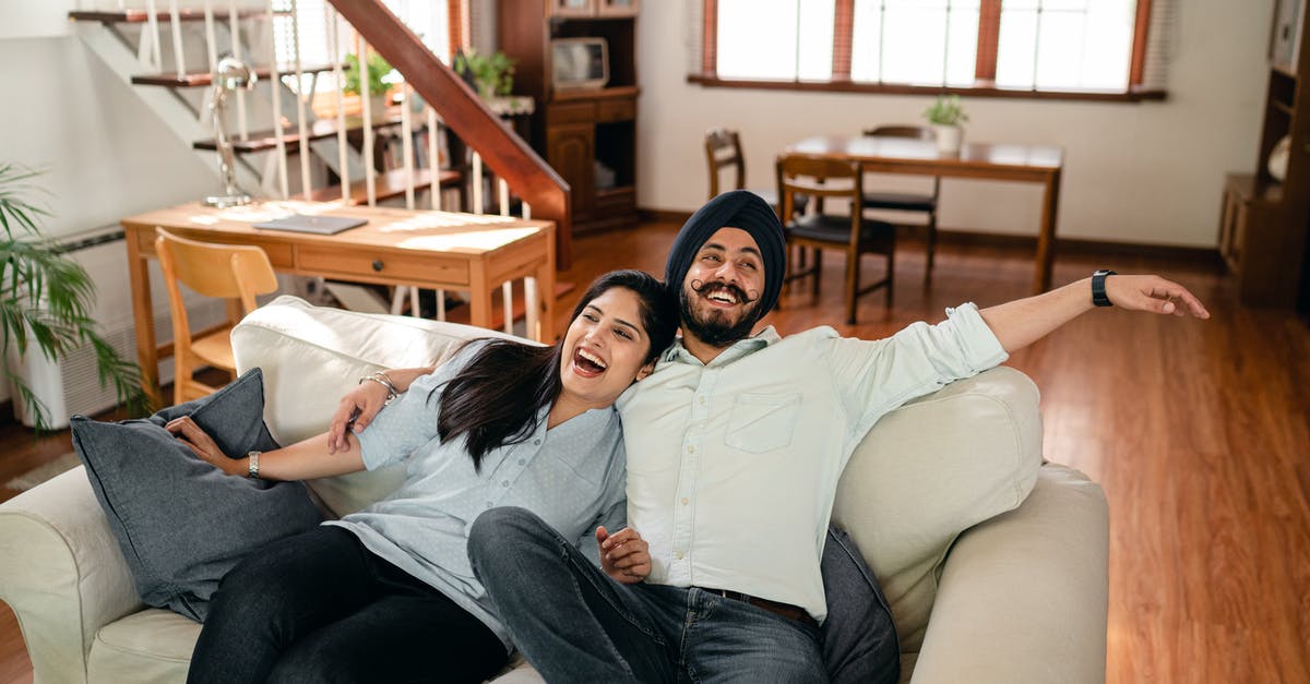 Does Lt. Columbo have an imaginary wife? - From above of cheerful young Indian couple in casual wear laughing and hugging each other while relaxing on cozy sofa in contemporary living room