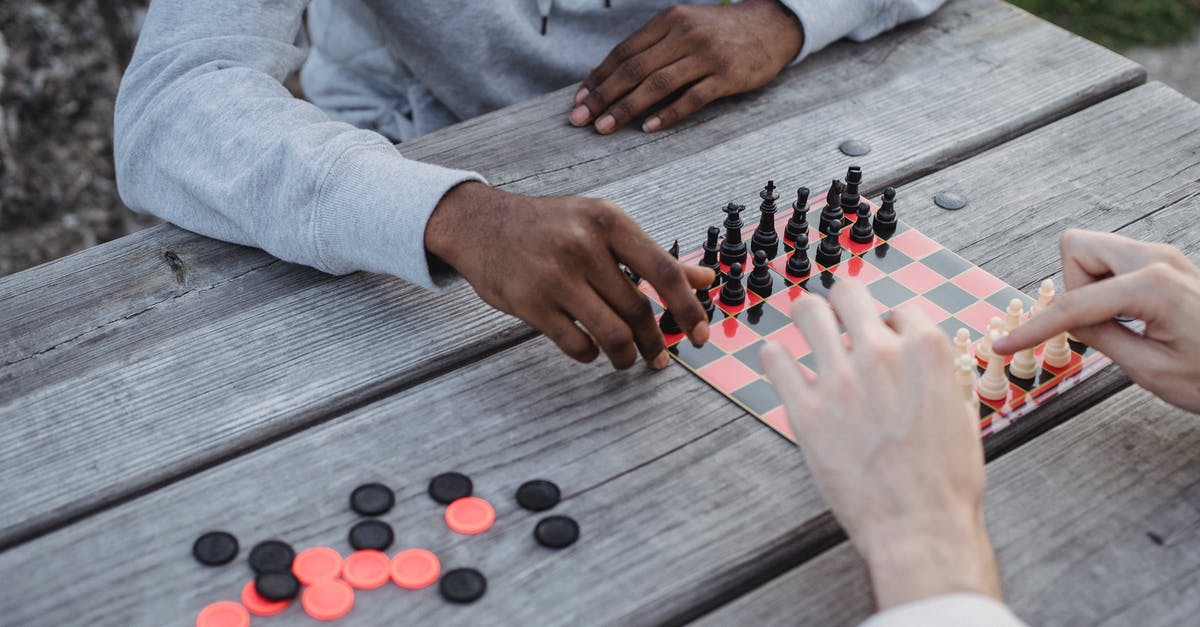 Does time-leaping move your mind or your body? - From above of crop unrecognizable multiethnic male friends sitting at wooden table in park and playing chess