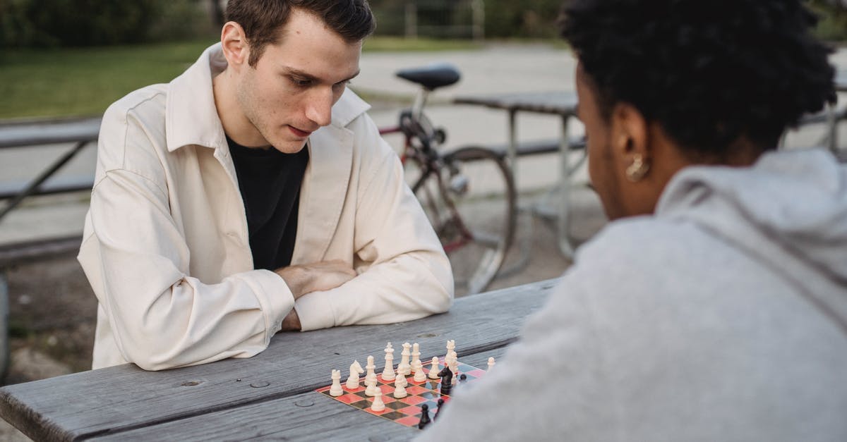 Does time-leaping move your mind or your body? - Concentrated young guy in casual clothes thinking while playing chess game with anonymous African American male friend in park