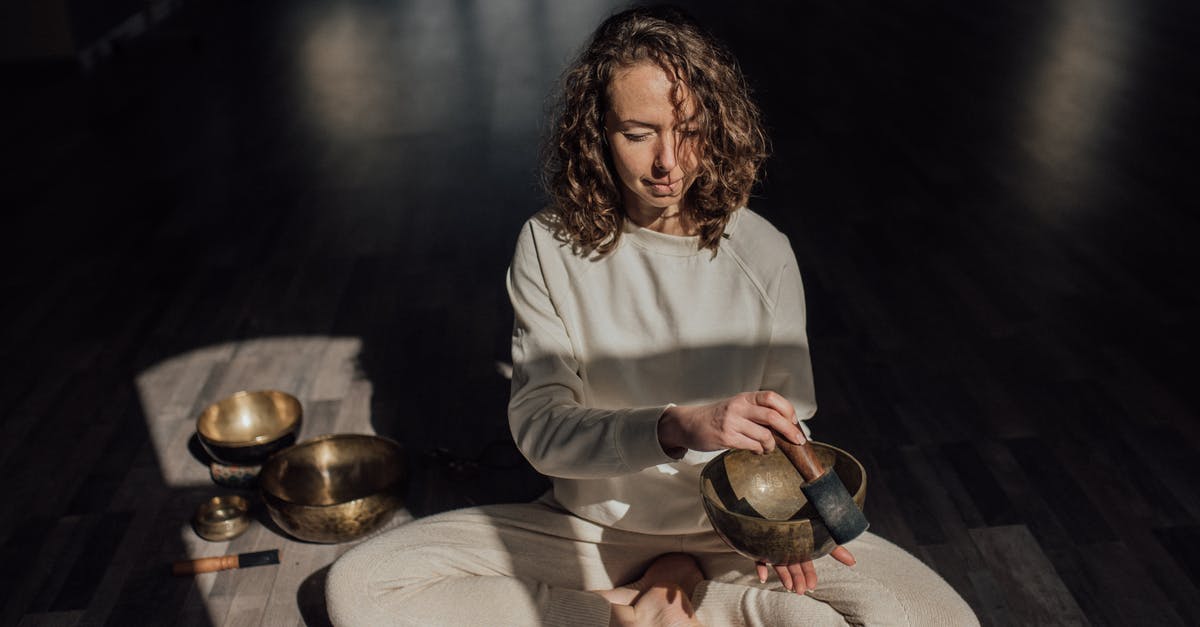Does Tom Ellis perform his own musical numbers? - Female sound therapist sitting with crossed legs on parquet while playing singing bowl with mallet during meditation practice