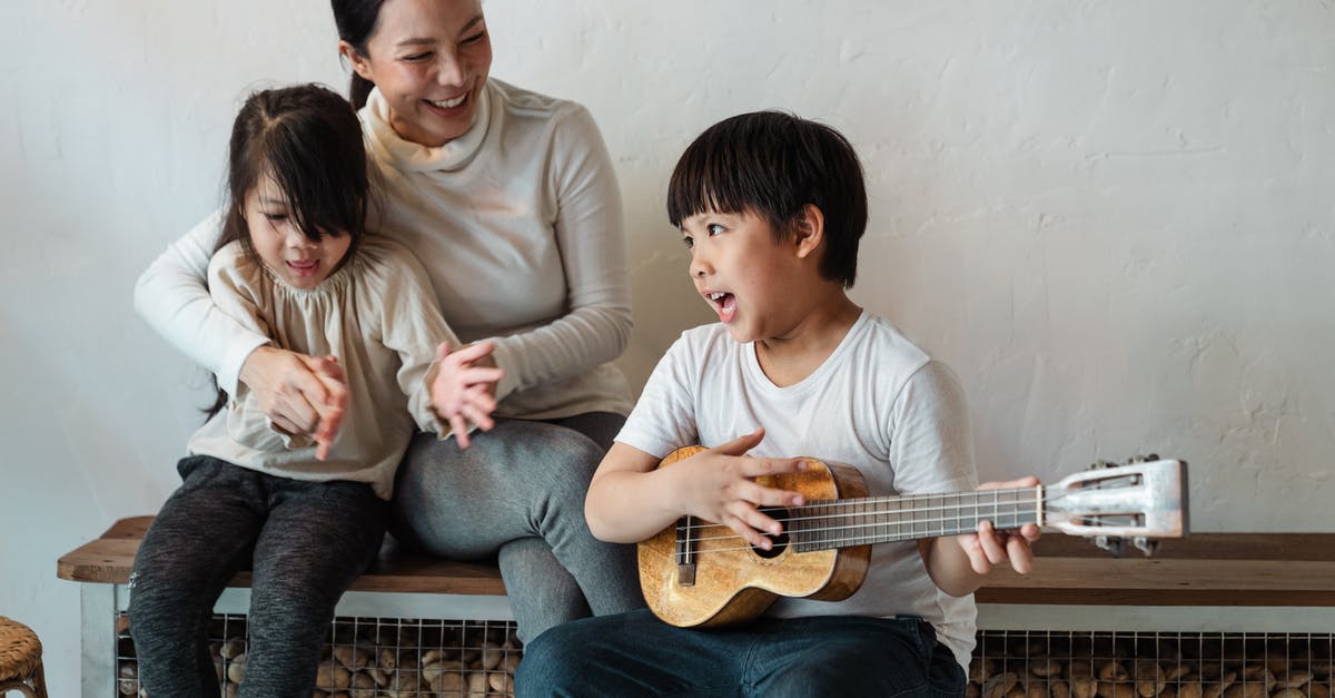 Does Tom Ellis perform his own musical numbers? - Ethnic boy playing ukulele while sitting with mother and sister