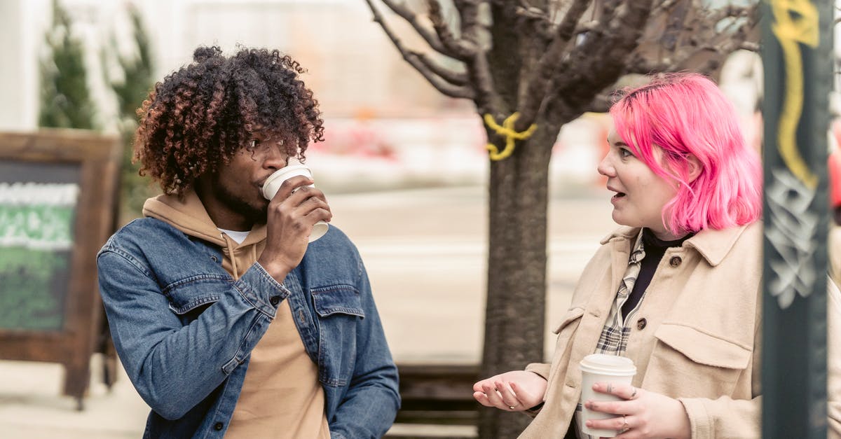 Explain Bonpensiero's appearance in this scene? - Trendy young informal female millennial with pink dyed hair in stylish outfit sitting on bench and chatting with African American male friend during coffee break in city park