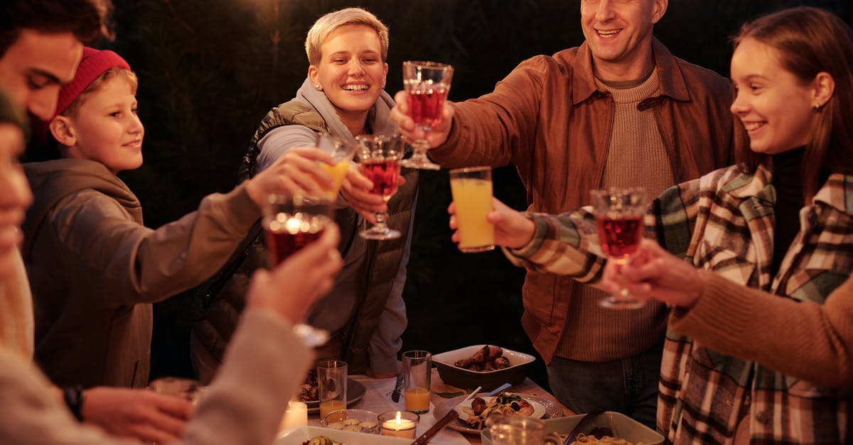 Exposing Alcohol in films to kids or teens - Laughing friends with kids spending time in backyard at night enjoying dinner with garlands and clinking glasses