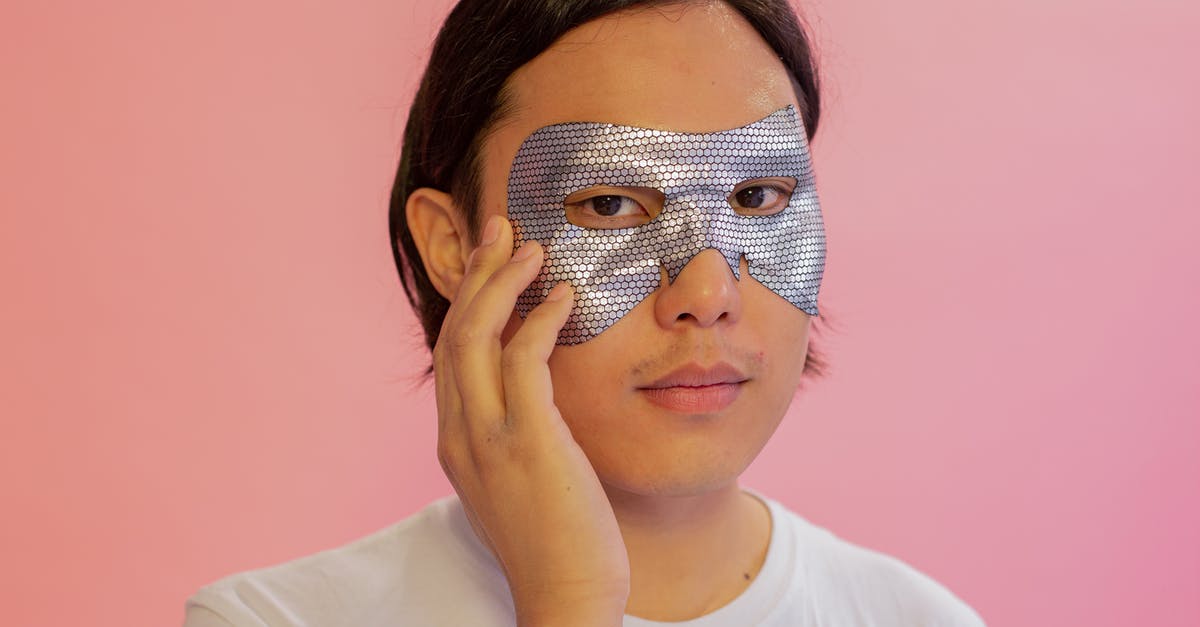 Eye part mask of Spider-Man and Deadpool - Emotionless young Asian male in white shirt with cosmetic eye mask touching face and looking at camera against pink background