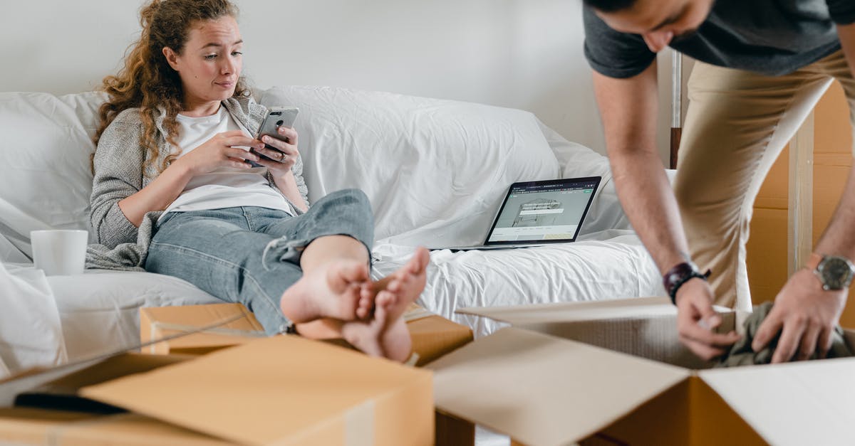 First use of on-screen text messages, like in Sherlock and House of Cards - Barefoot female in casual wear sitting with crossed legs on sofa with open laptop while using social media on cellphone and crop male partner getting clothes out of cardboard box