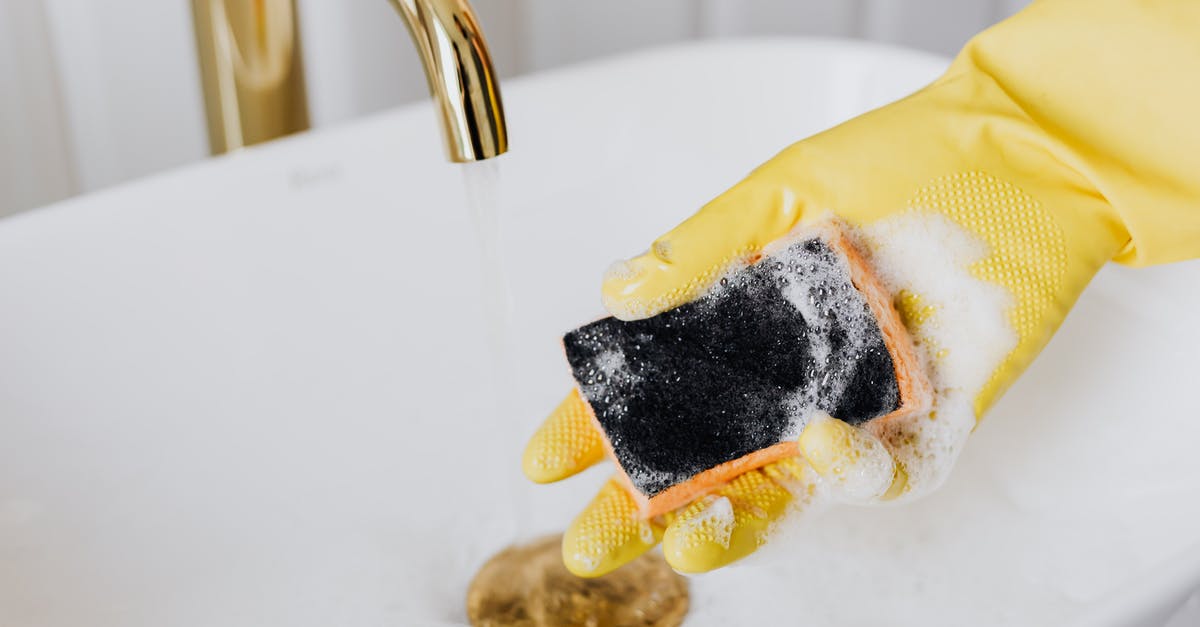 Has a streaming service original program ever reached 100 episodes? - Crop faceless person in yellow latex protective glove using detergent and sponge while washing surface of white sink in bathroom