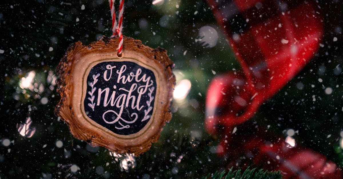Has Carol become unrealistically unhinged? - Wooden bauble with O Holy Night inscription hanging on green Christmas tree decorated with red ribbon on snowy day