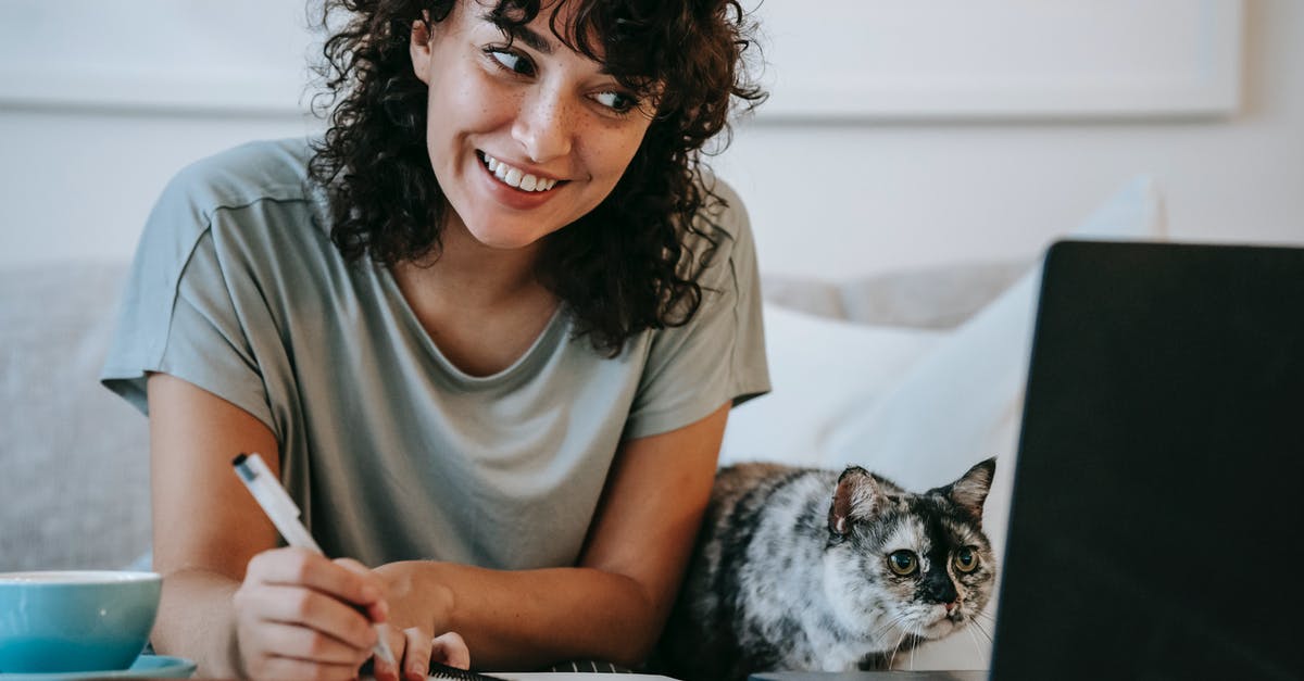 Has Hollywood used the same recording of cat meows and screeching in multiple movies? - Crop young positive female smiling and taking notes in organizer while cat watching on netbook at table at home