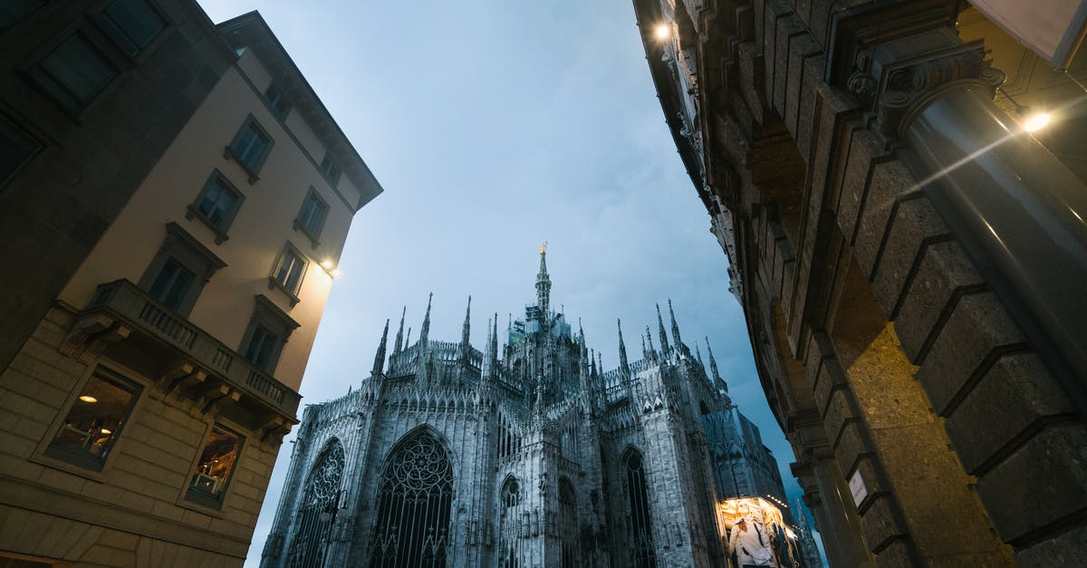 Has Stefano Di Mera ever been in the Italian Mafia? - Low angle of city buildings and Milan Cathedral of Nativity of Saint Mary with glowing facade advertising on cloudy dusky evening