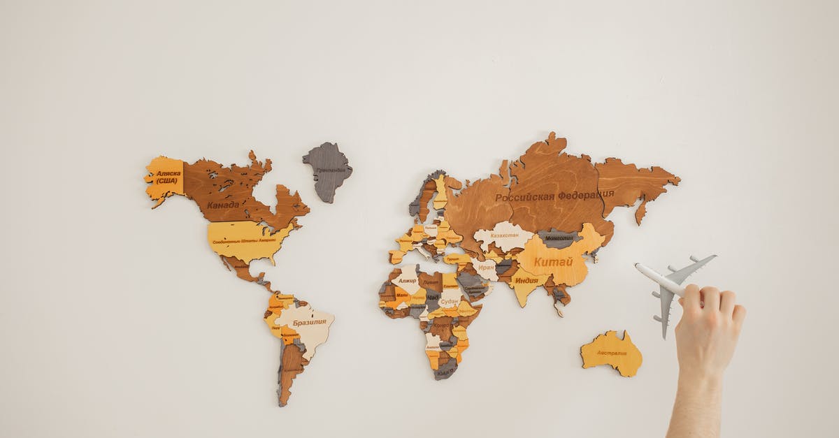 Has the name "White Portuguese" a deeper meaning? - Crop anonymous traveler with toy aircraft over decorative wooden world map with country names on white background in light room